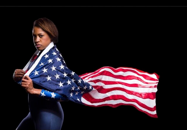 Woman draped in an American flag like a cape, standing against a dark background.