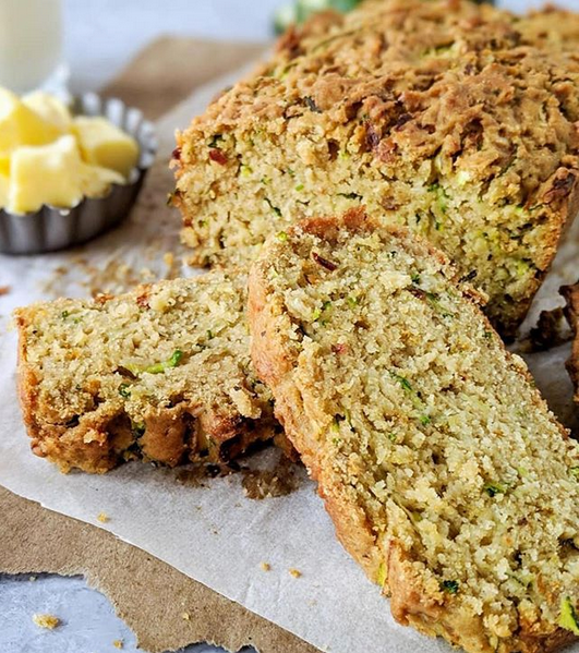 Sliced loaf of zucchini bread on parchment paper with butter and a glass of milk nearby.