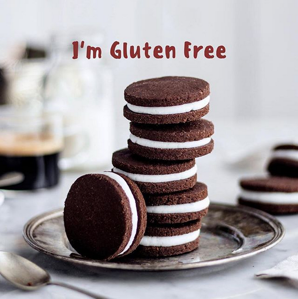 Stack of chocolate sandwich cookies with white cream filling on a plate, one cookie leaning in front, with text reading “I’m Gluten Free.”
