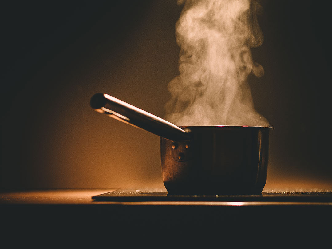 Small pot on a stovetop with steam rising, lit by warm, low lighting.
