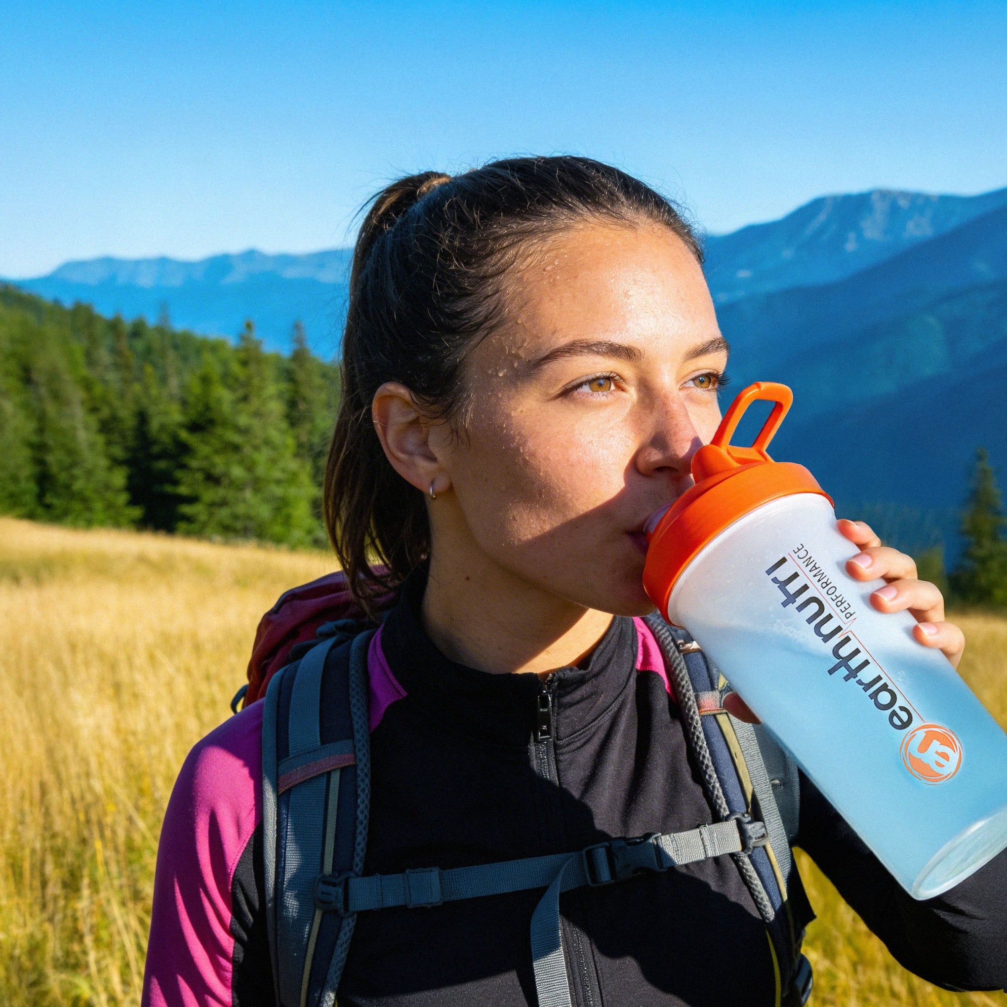 Person drinking from a water bottle with mountains in the background
