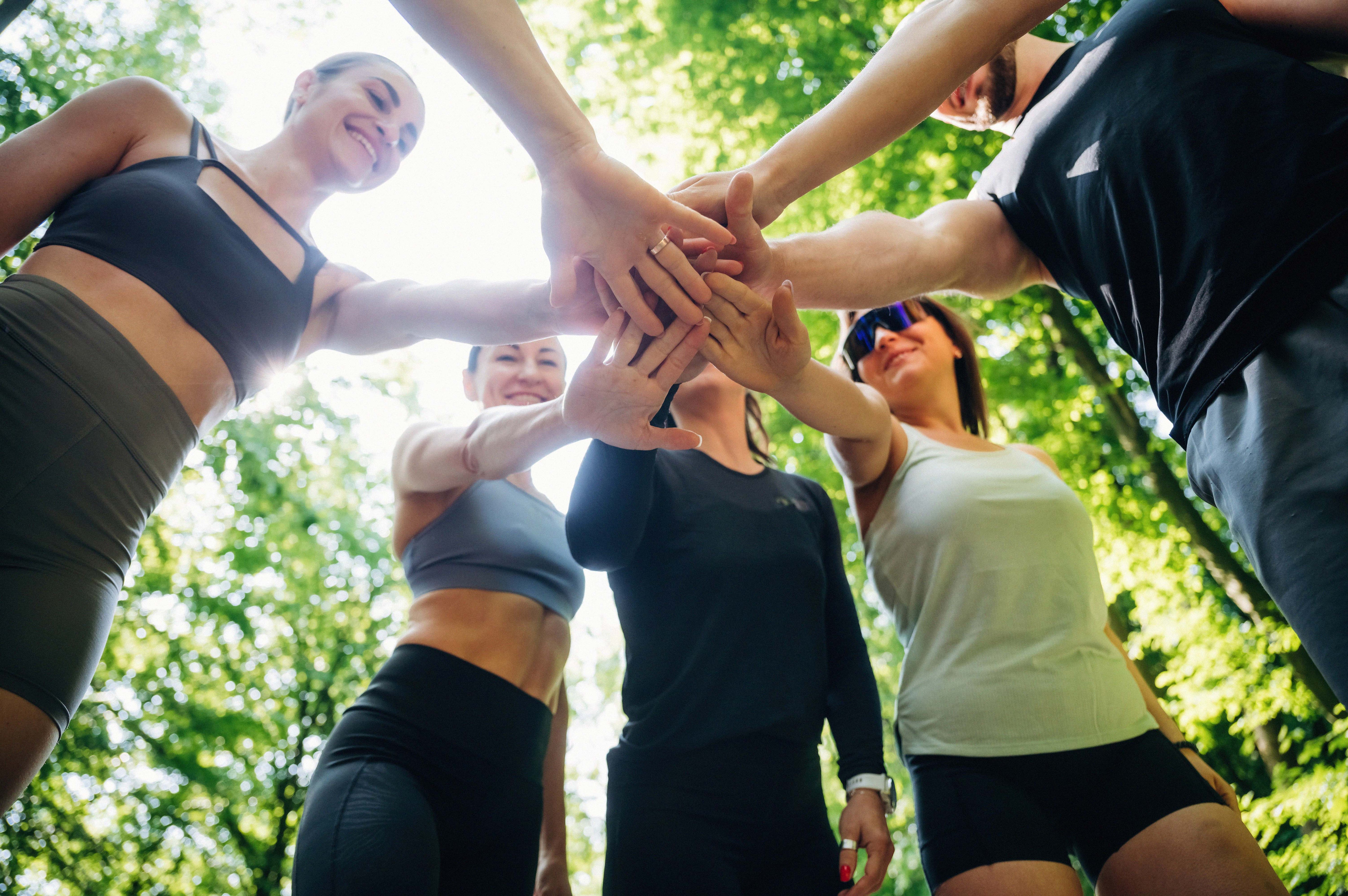 Group of althetes standing in a circle and putting their hands on top of one another in the center.