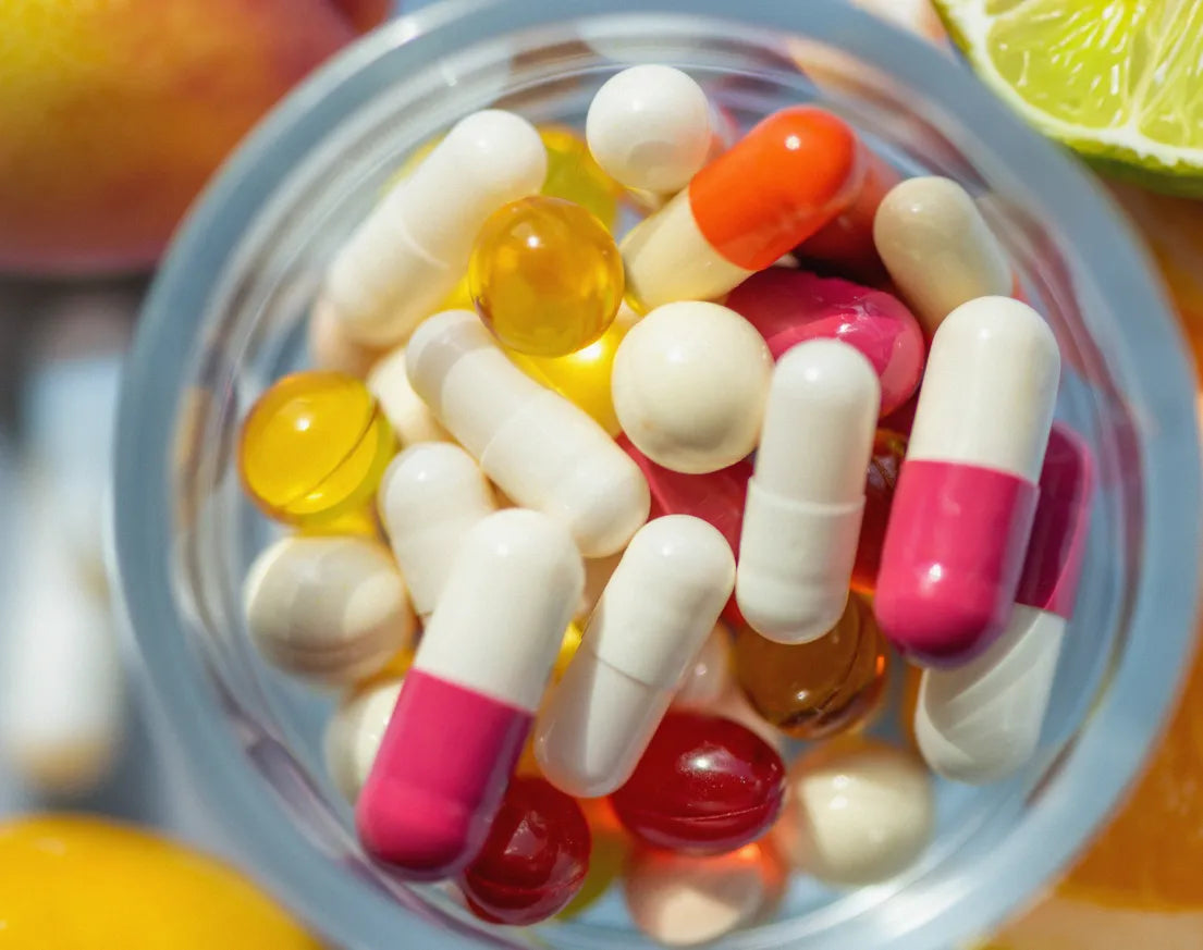 A glass filled with colorful capsules and softgel pills.