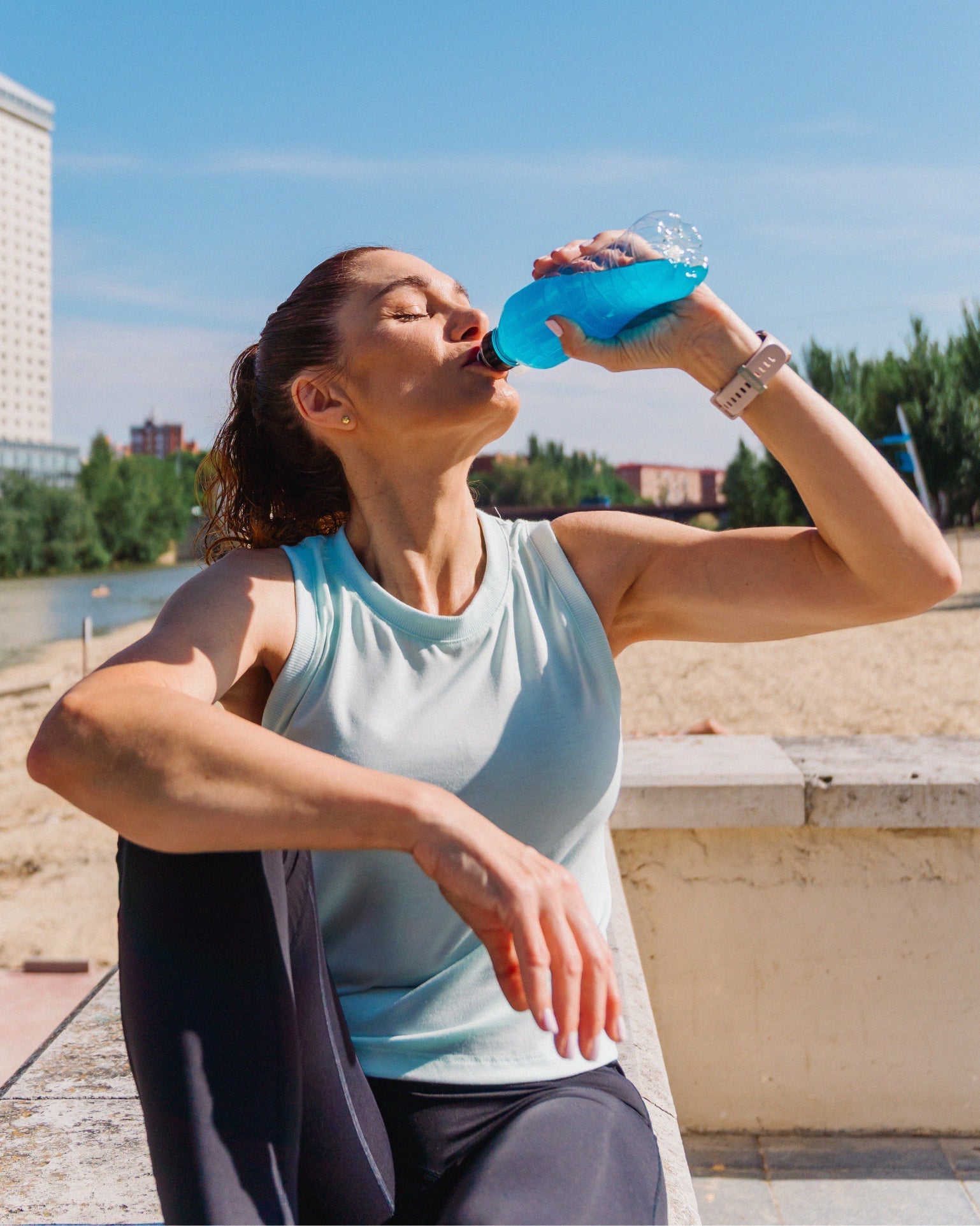 Woman outdoors drinking a blue sports hydration beverage after exercise on a sunny day.