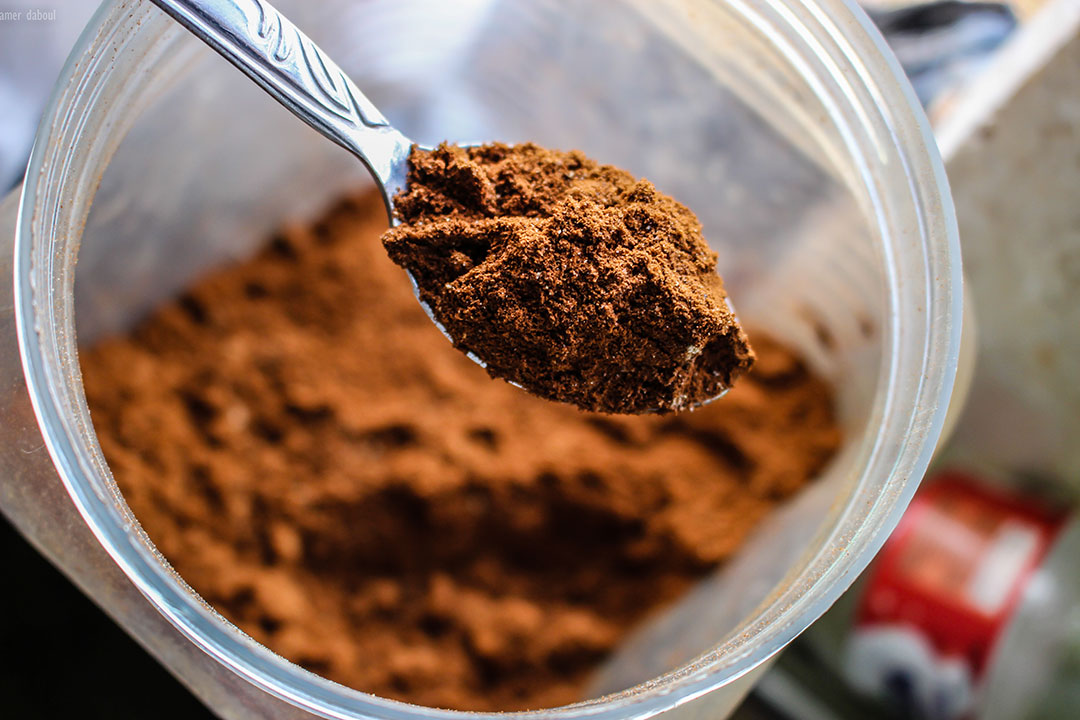 Spoonful of brown powder held above an open container filled with the same powder.