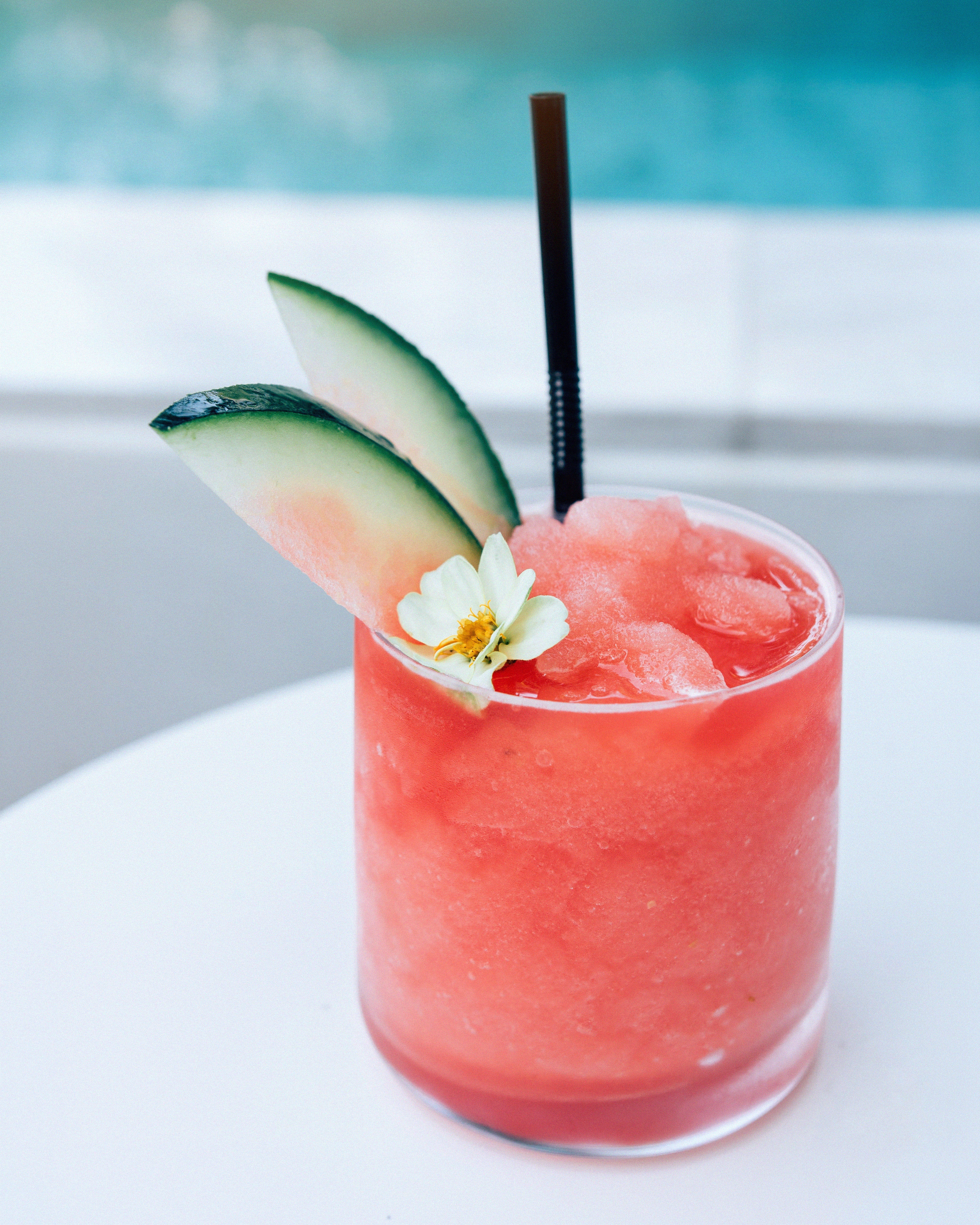 Watermelon slushie garnished with melon slices and a flower, served over ice beside a pool.