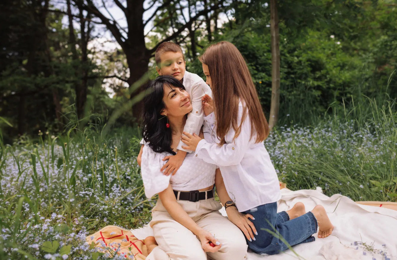 A woman sits in a meadow with two children, sharing a warm, joyful moment together. 