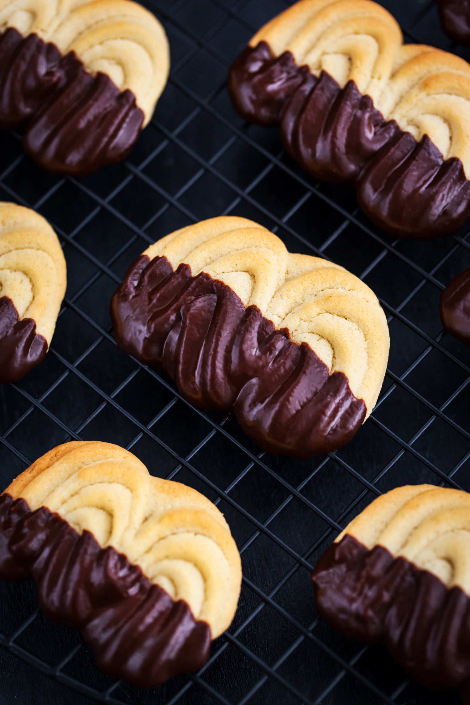 Orange Zest shortbread cookies partially dipped in chocolate ganache, arranged on a cooling rack.