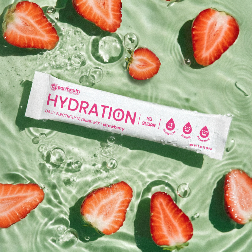 Earthnut Hydration drink mix packet surrounded by sliced strawberries on a green background